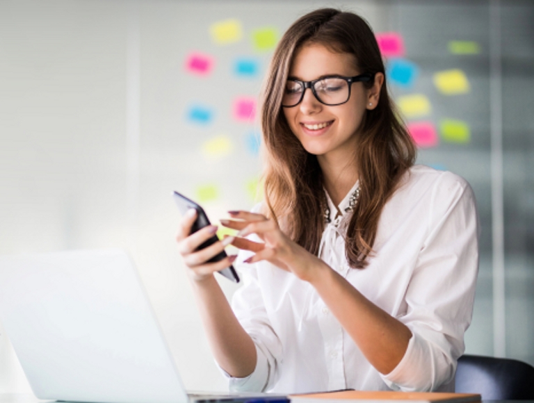 Profesional sonriente utiliza su smartphone en un entorno de oficina moderno.