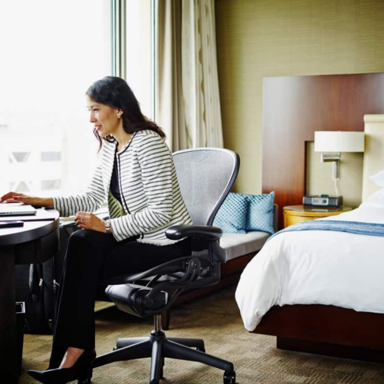 Una profesional en viaje de negocios trabaja en su laptop sentada en su habitación del hotel.