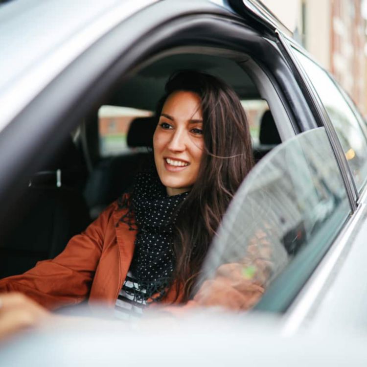 Una mujer sonriente conduce un auto alquilado con la ventanilla baja.