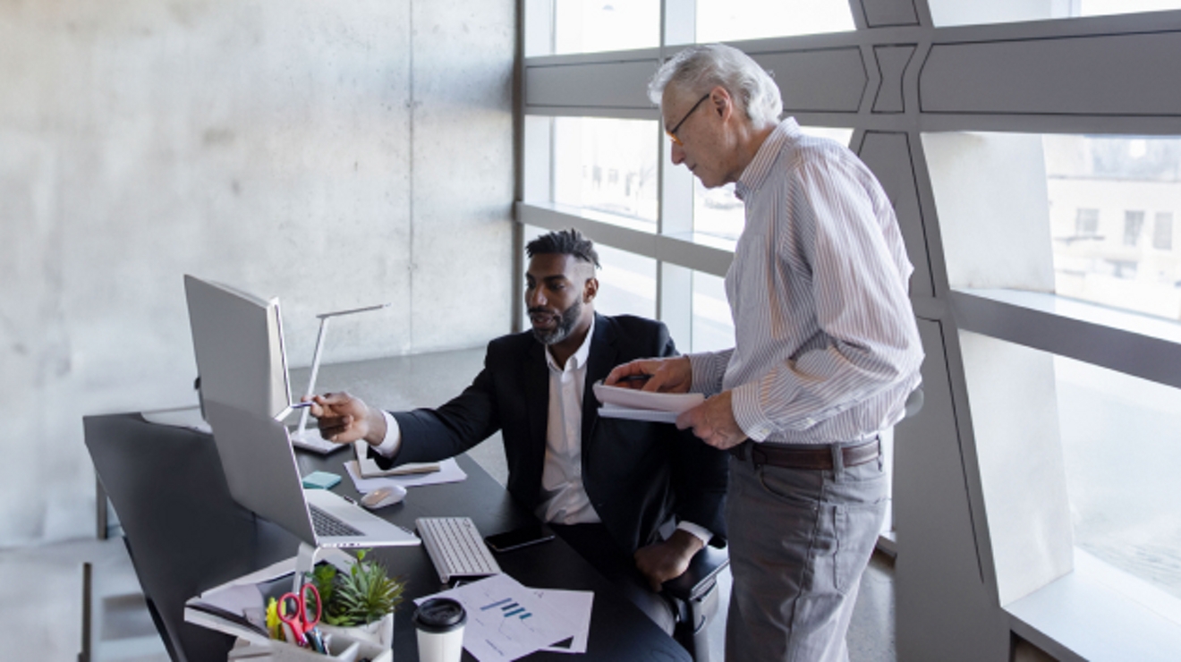 Dos empleados del gobienro colaboran a través de varias computadoras en la oficina.