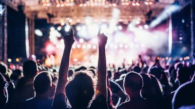 Vista desde atrás de un público que disfruta de un concierto, a contraluz de la colorida iluminación del escenario.