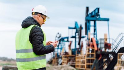 Profesional con equipo de seguridad trabaja con una tablet en una zona de perforación.