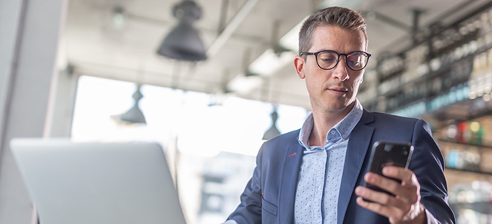 Un hombre mira un teléfono con una laptop abierta delante