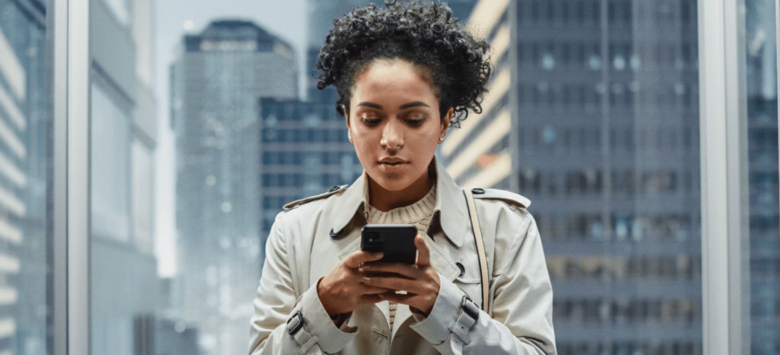 Una joven profesional de servicios financieros con su smartphone en un edificio de oficinas de vidrio en la ciudad.