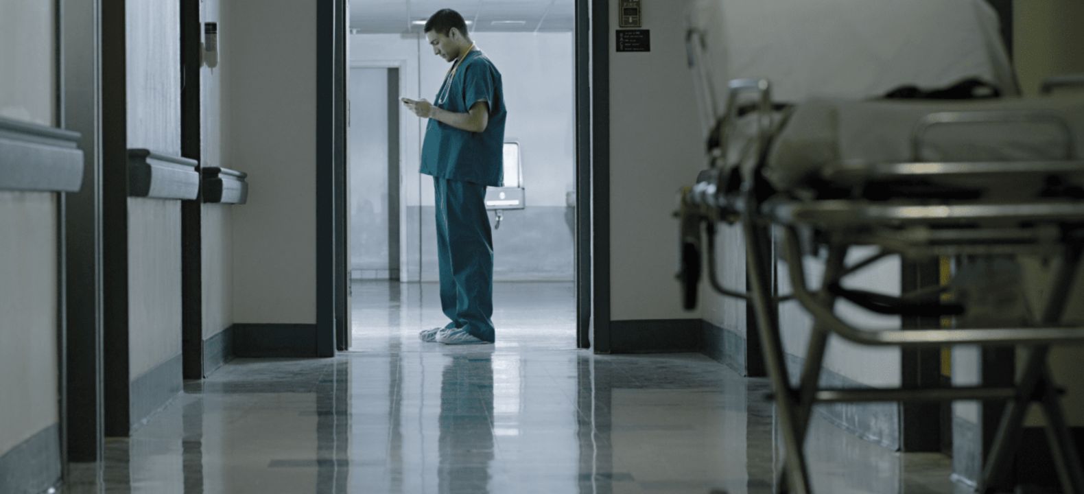 Un profesional sanitario con su smartphone al final del pasillo de hospital.