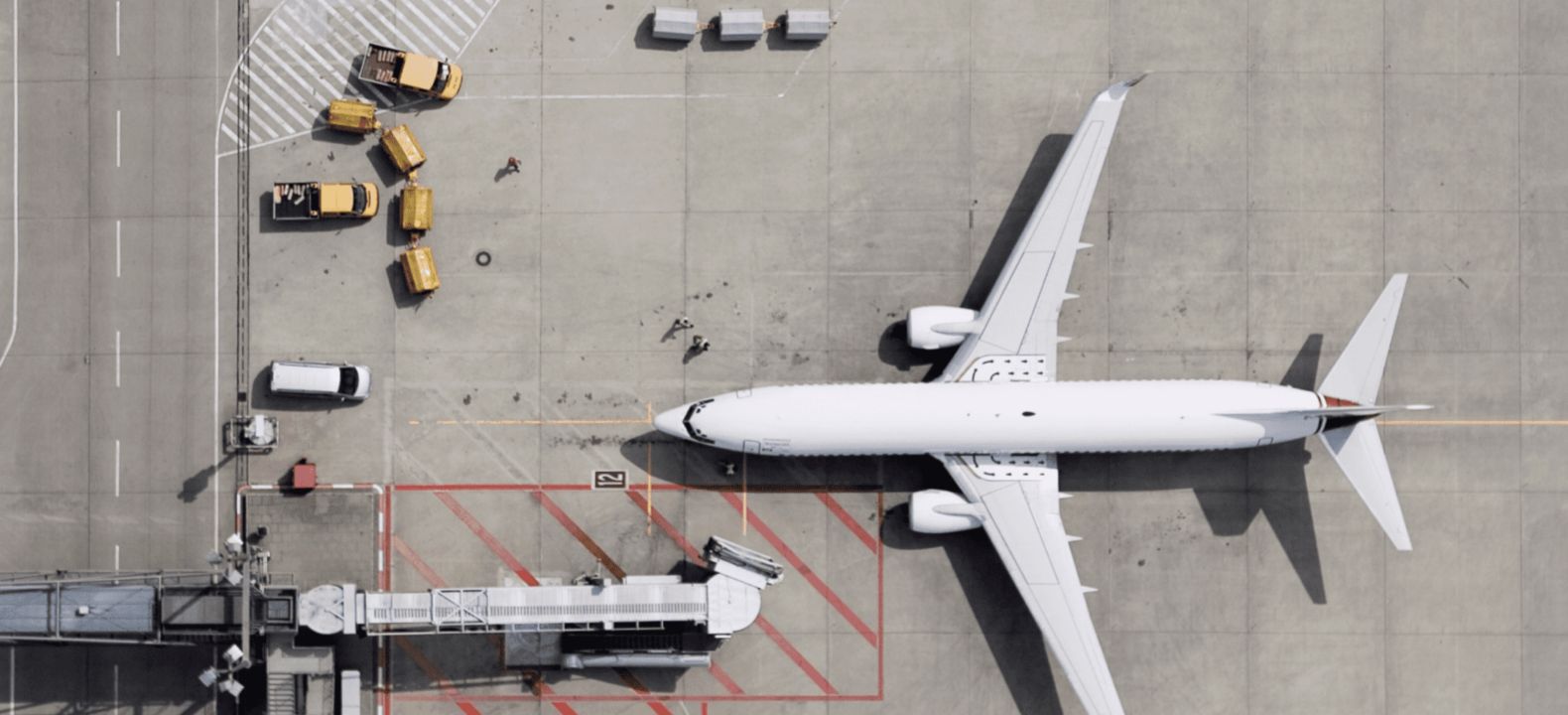 Vista aérea de la puerta de un aeropuerto, que incluye una pasarela de acceso, camiones y un avión de pasajeros.