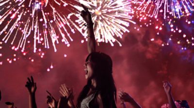 Multitud de personas en un concierto con fuegos artificiales de fondo.