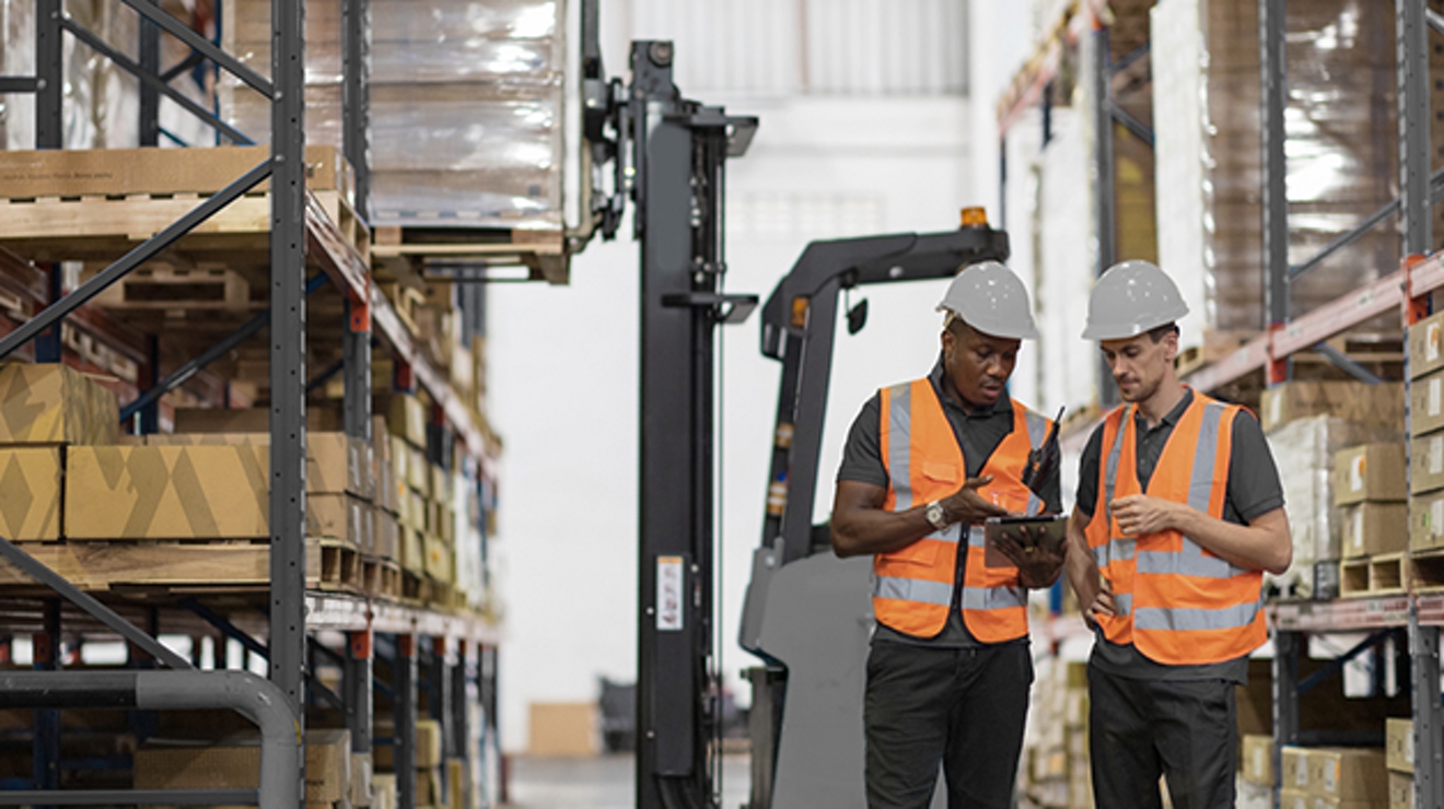 Trabajadores en un almacén con cascos y chalecos de seguridad naranjas