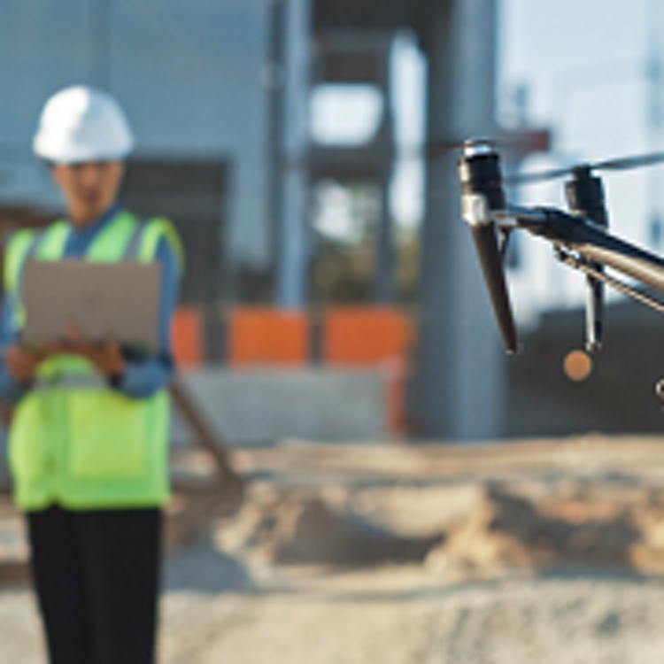 Trabajador de la construcción sostiene una tablet mientras opera un dron frente a él