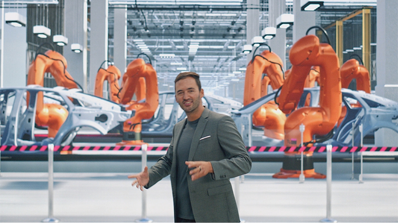 Un hombre con traje gris delante de robots que ensamblan vehículos