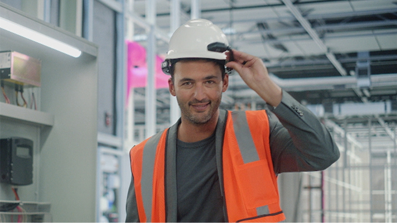 Un hombre con chaleco de seguridad naranja y casco blanco sonriendo