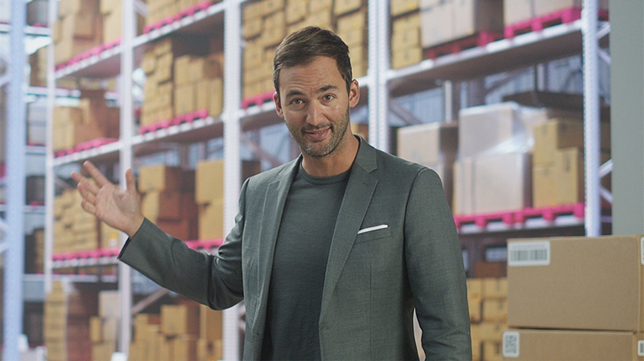 Un hombre con traje gris delante de cajas apiladas en un almacén