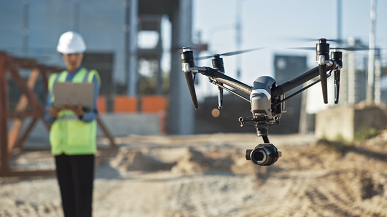 Un hombre con chaleco de seguridad amarillo sostiene una computadora en segundo plano con un dron enfocado