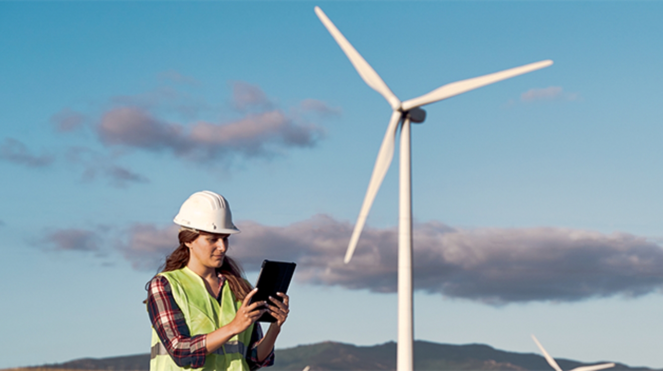 Mujer con casco blanco enfrente de una turbina eólica