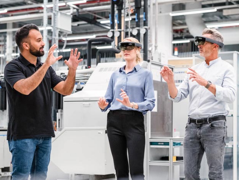 Una persona en un entorno industrial da indicaciones a otras dos personas que están usando gafas de RV