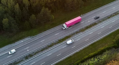 Vista aérea de un camión semirremolque que transporta un remolque magenta y circula por una autopista