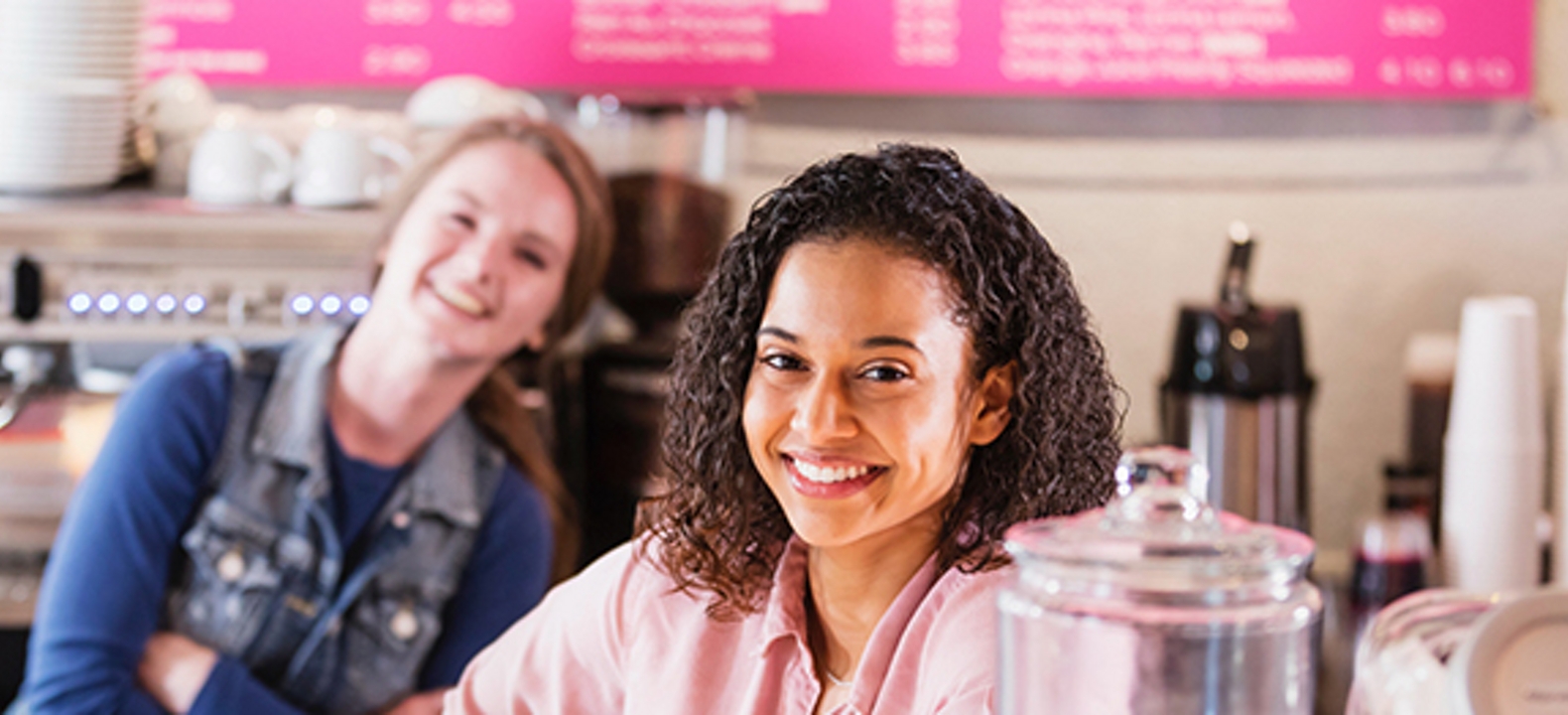 Dos mujeres sonrientes paradas tras un mostrador en una cafetería.