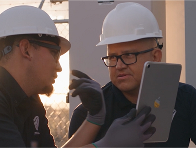 Dos hombres con casco blanco hablando y viendo un Apple iPad.