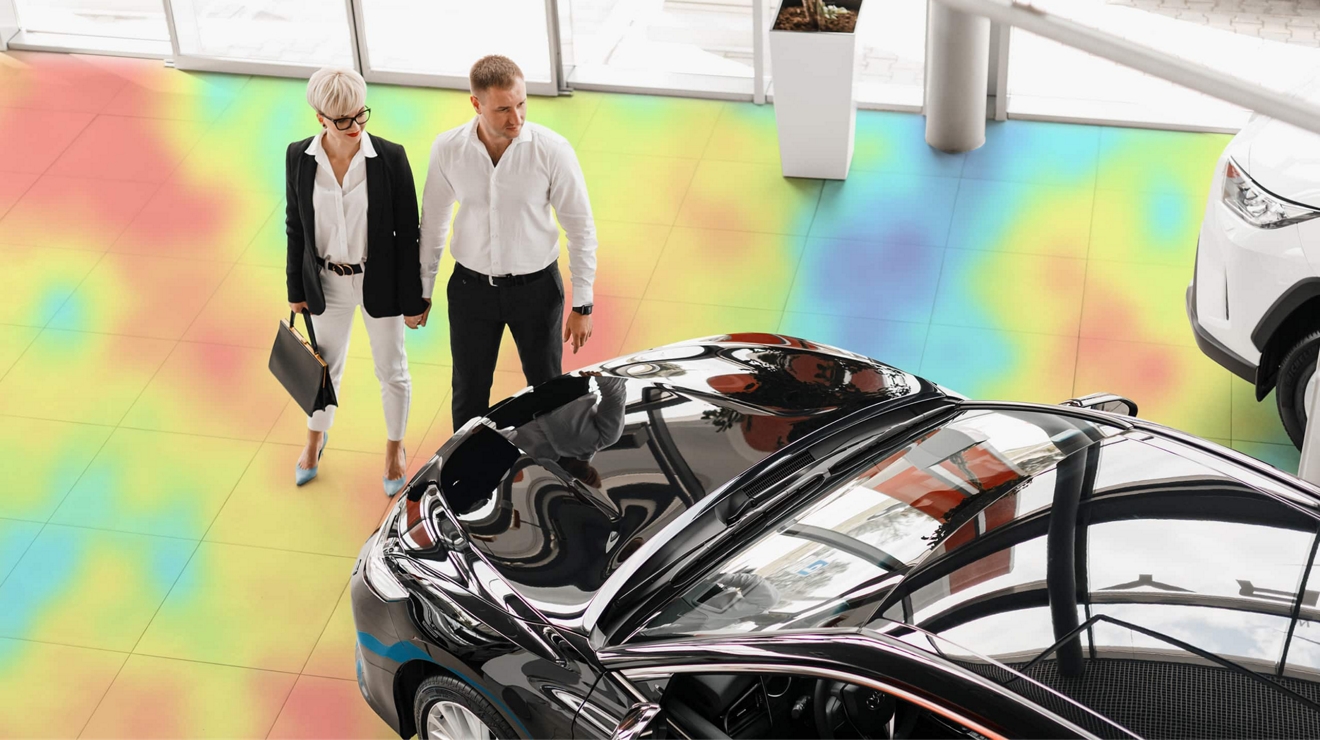 Una pareja de pie dentro de un mapa de calor mirando un vehículo en la sala de exposición de un concesionario de autos.