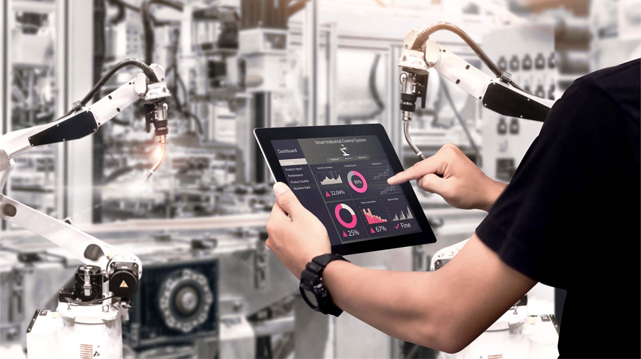 Trabajador de una fábrica utiliza su tablet 5G para consultar los datos de rendimiento de un dispositivo robotizado.