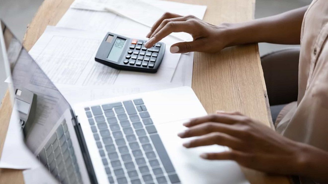 Un profesional de los negocios trabaja en una laptop con una mano y en una calculadora con la otra.