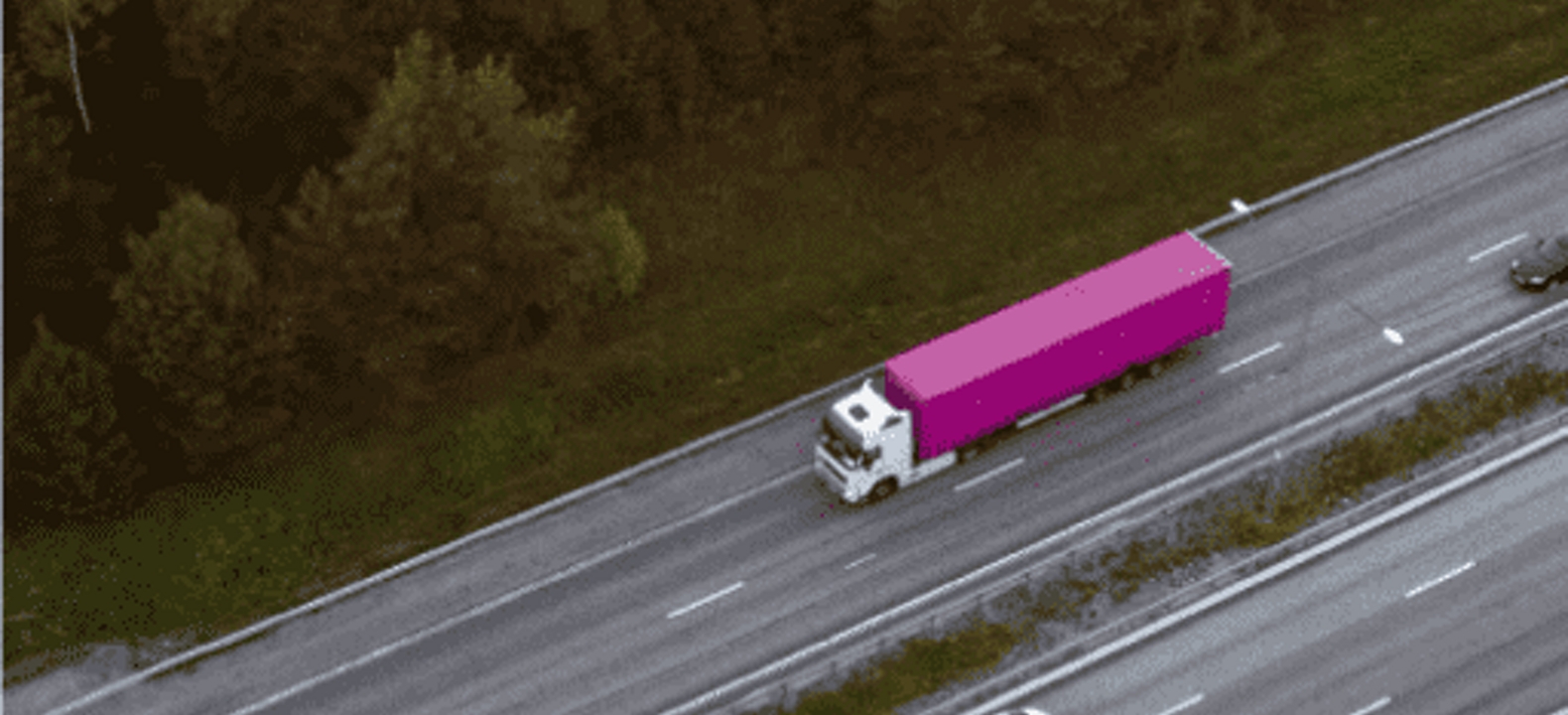 Un camión semirremolque magenta viajando por una carretera.