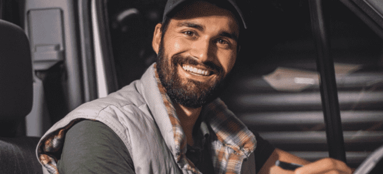 Chofer sonríe a la cámara mientras completa documentación en el asiente del conductor de su vehículo.