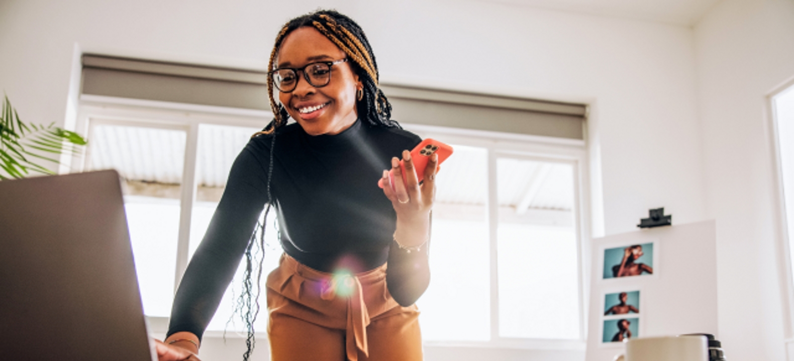 Mujer joven sonriente usa su laptop y smartphone simultáneamente.