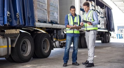Dos trabajadores con chalecos de alta visibilidad discuten sobre documentación junto a un semirremolque.