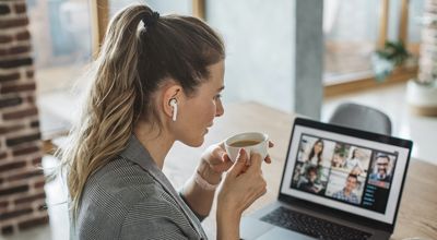 Mujer con el cabello recogido y audífonos sentada mirando una videoconferencia en la pantalla