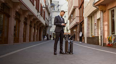 Un profesional de los servicios financieros con una maleta consulta su smartphone en plena calle peatonal.