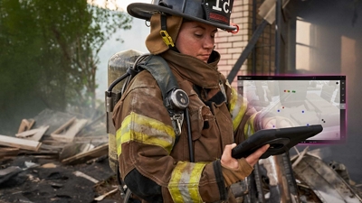 Una bombera con equipo completo utiliza una tablet para localizar a los bomberos en un bloque de edificios del centro de la ciudad.