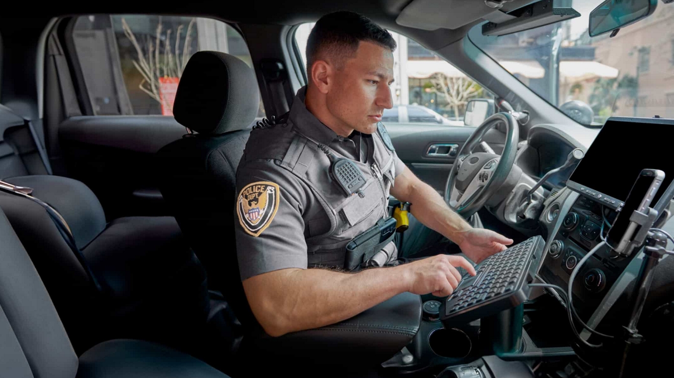 Un agente de policía en un vehículo envía datos a través de una conexión móvil de alta velocidad utilizando un smartphone y un teclado externo.