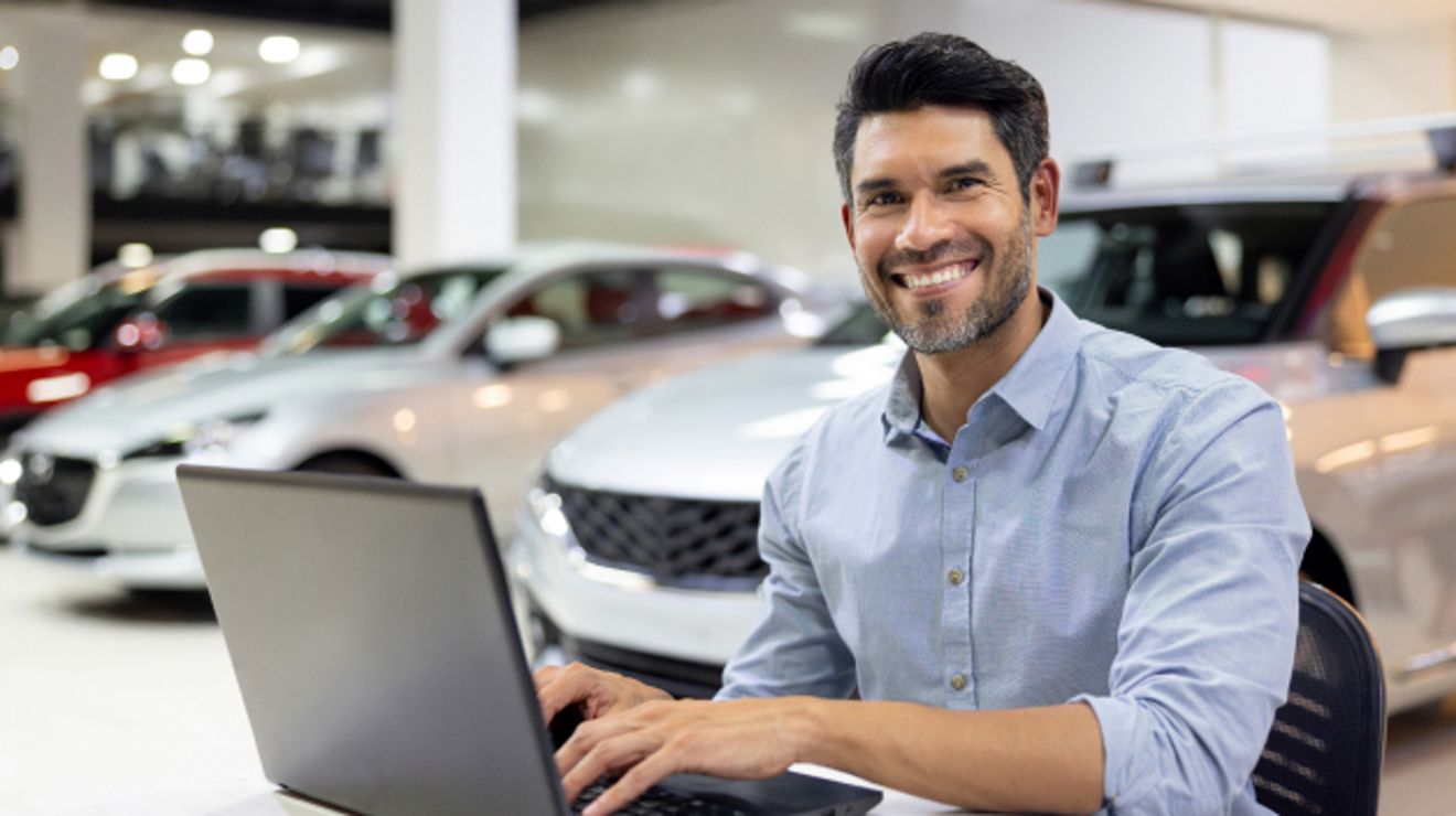 Un sonriente vendedor de un concesionario de automóviles ofrece un servicio al cliente eficiente a través de su laptop.