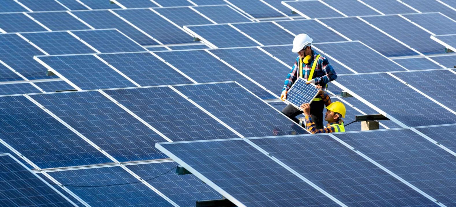 Un trabajador reemplaza un panel solar en una granja solar mientras lo ayuda otro miembro del equipo.