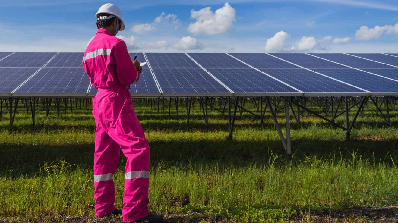 Un técnico energético escribe en su tablet mientras revisa los paneles de una instalación de energía solar.