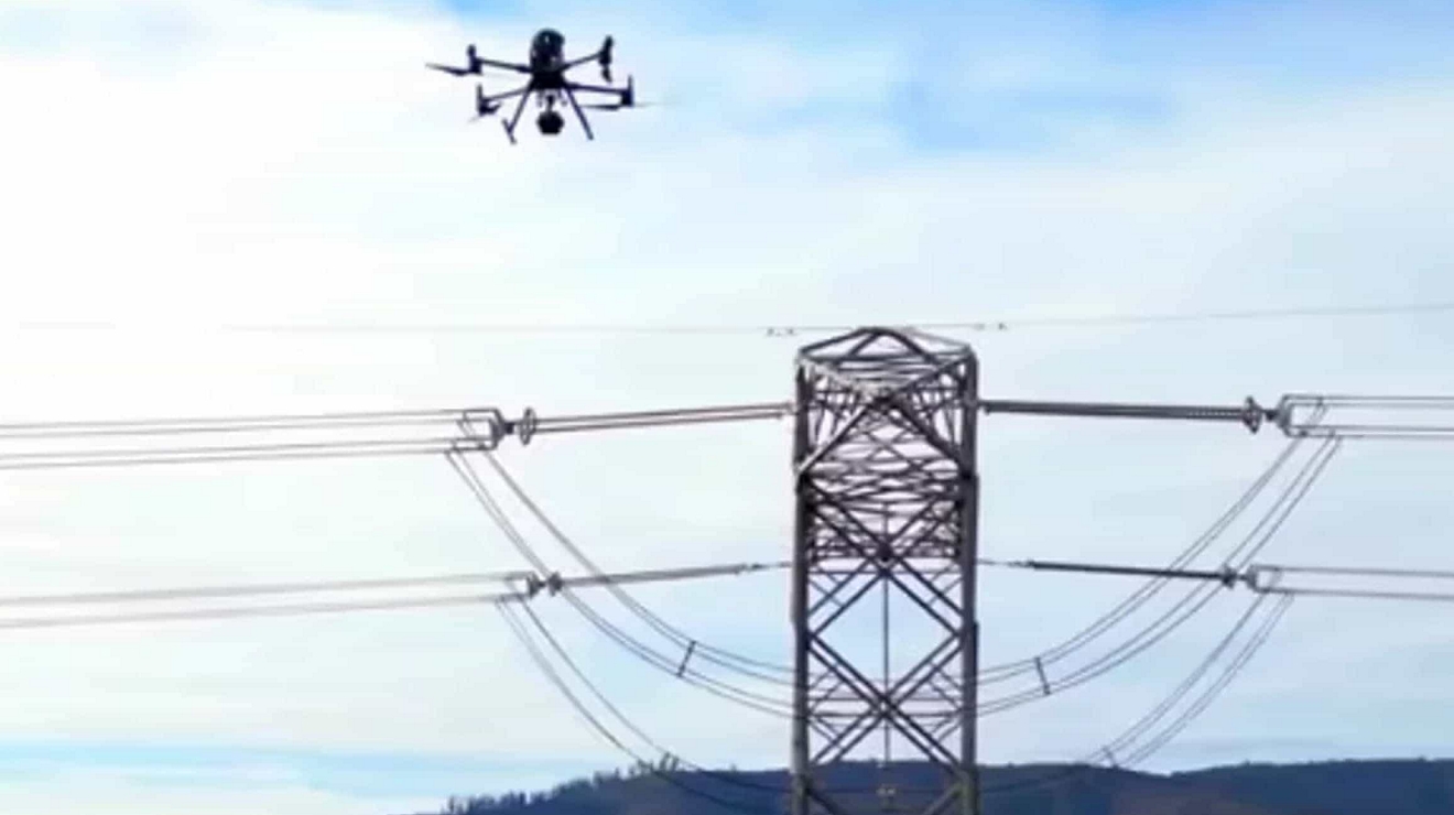 ​​​​​​​Un dron conectado pasa sobre una torre de tendido eléctrico, utilizando visión computarizada para inspeccionarla.