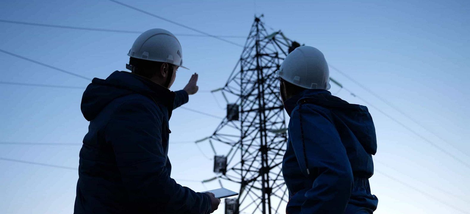 Trabajadores energéticos consultan una tablet con 5G mientras observan las líneas de transmisión.
