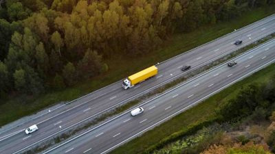 Vista aérea de una autopista de cuatro carriles por la que circulan tres autos y un semirremolque.