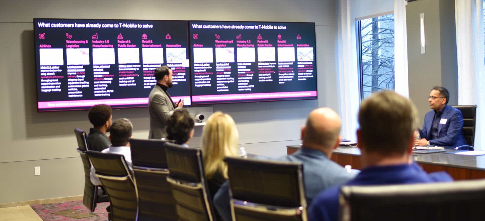 Un experto de T-Mobile utiliza dos pantallas de gran formato para presentar las soluciones de T-Mobile a un grupo de ejecutivos.