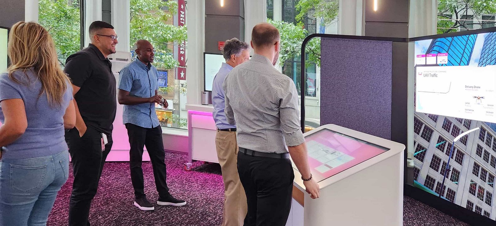 Un experto de T-Mobile dirige una demostración interactiva con un ejecutivo mientras un grupo se reúne para observarla.
