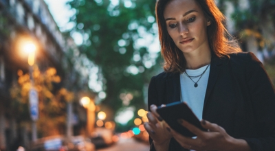 Una profesional de servicios financieros consulta su smartphone mientras camina por una calle de la ciudad.