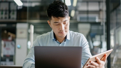 Un profesional de los servicios financieros trabaja a distancia con una laptop y una tablet.