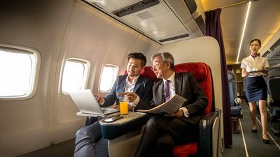 Dos profesionales trabajan juntos en una laptop conectada en clase business en un vuelo internacional.