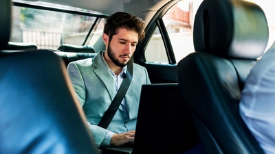 Un viajero de negocios trabaja con su laptop en el asiento trasero de un vehículo de viaje compartido.