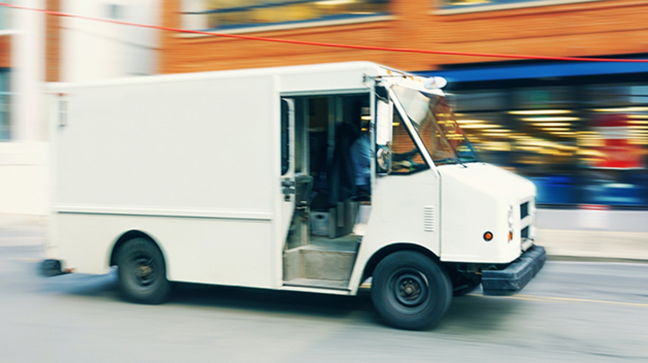 Camión de reparto blanco con un edificio naranja y azul desdibujado en el fondo