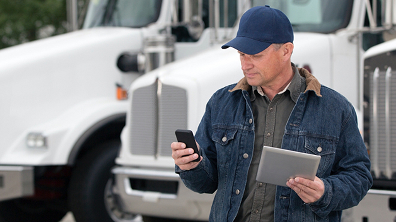 Hombre de pie cerca de unos camiones mirando un dispositivo móvil