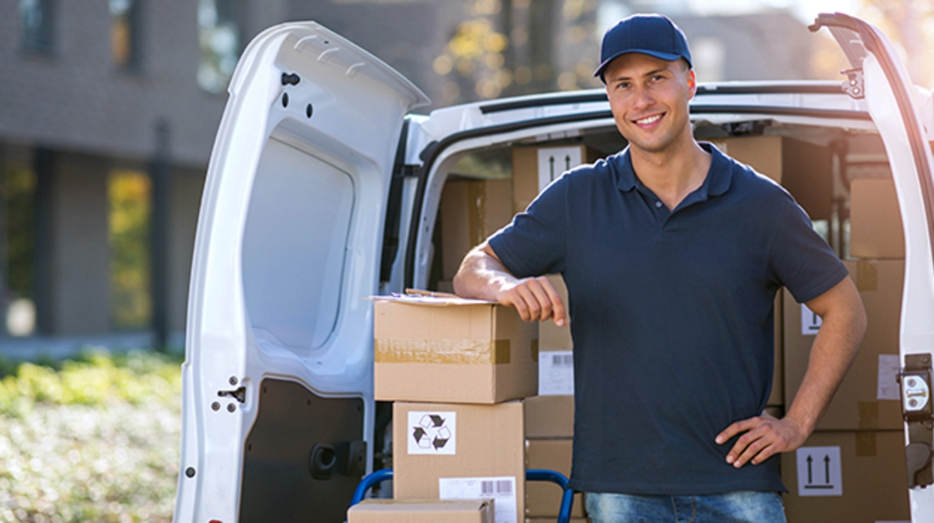 Hombre sonriente de pie junto a la parte trasera de un camión con el codo apoyado en unas cajas