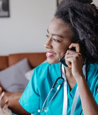 Una médica con bata y estetoscopio habla por su smartphone en una zona común.