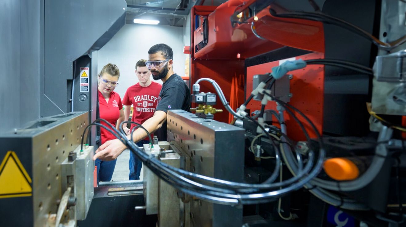 Dos estudiantes de la Universidad de Bradley observan a un instructor haciendo una demostración de maquinaria de alta tecnología.